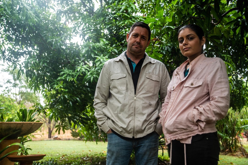 A man and a woman stand in their back yard looking at the camera