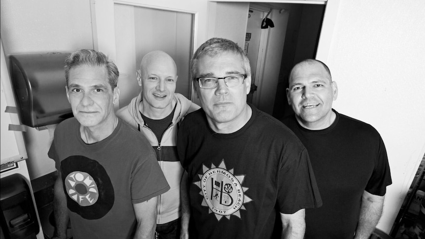 Four male members of Descendents smile at camera backstage in a green room