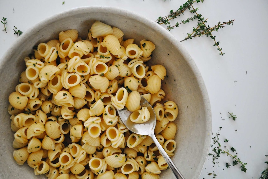 A bowl of cooked pasta shells with thyme vinaigrette mixed through to marinate, the base of a vegetarian pasta salad.