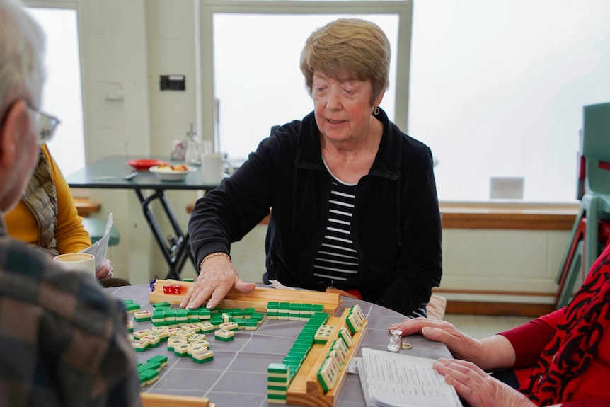 A woman sits at a table with three others, playing majong