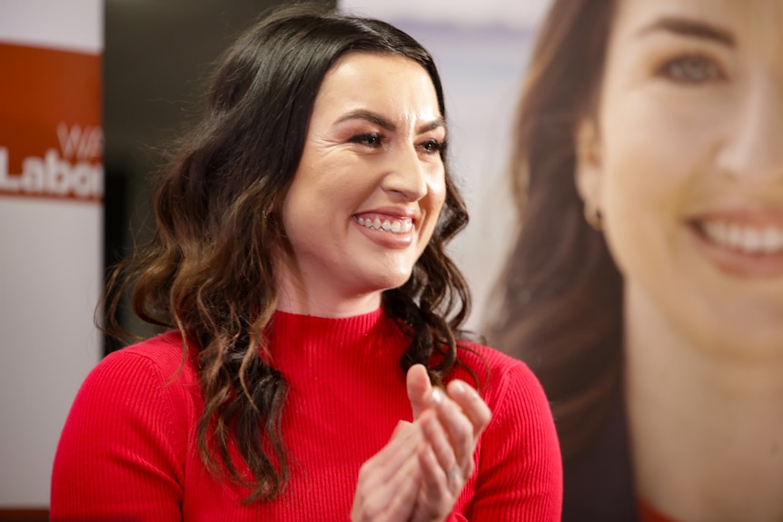 A woman in a black dress smiles and claps her hands.