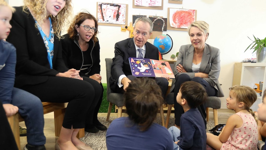 Bill Shorten reads a book to children sitting on the floor below him. He's surrounded by his Labor colleagues