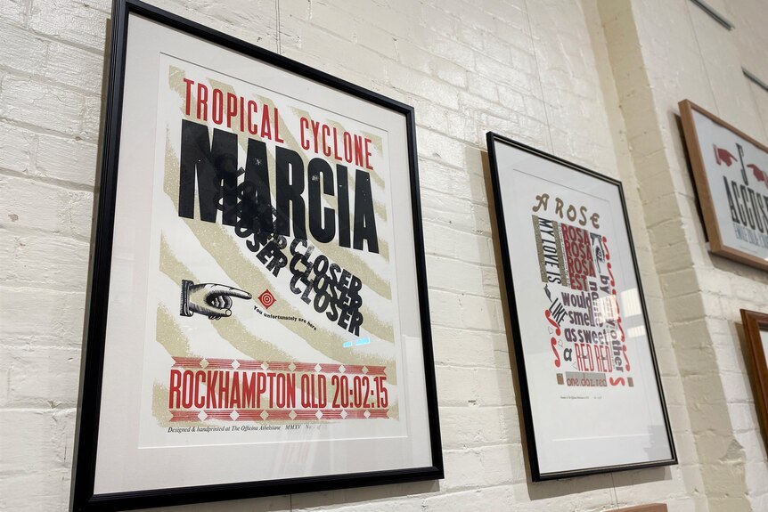 A framed graphic poster hangs on a wall, it says "tropical cyclone marcia' with Rockhampton, QLD below