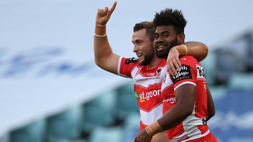 Euan Aitken points a finger on his right hand to the sky with his left arm around Mikaele Ravalawa after a Dragons try.