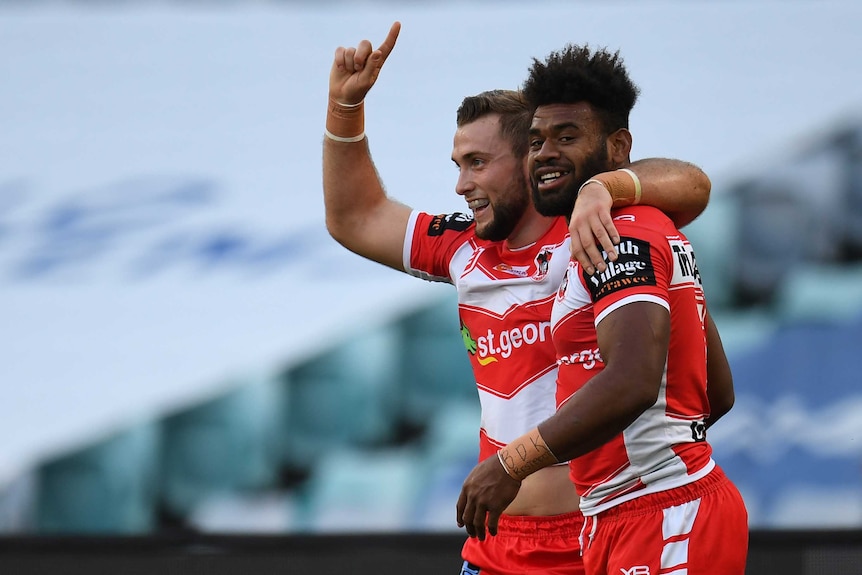 Euan Aitken points a finger on his right hand to the sky with his left arm around Mikaele Ravalawa after a Dragons try.