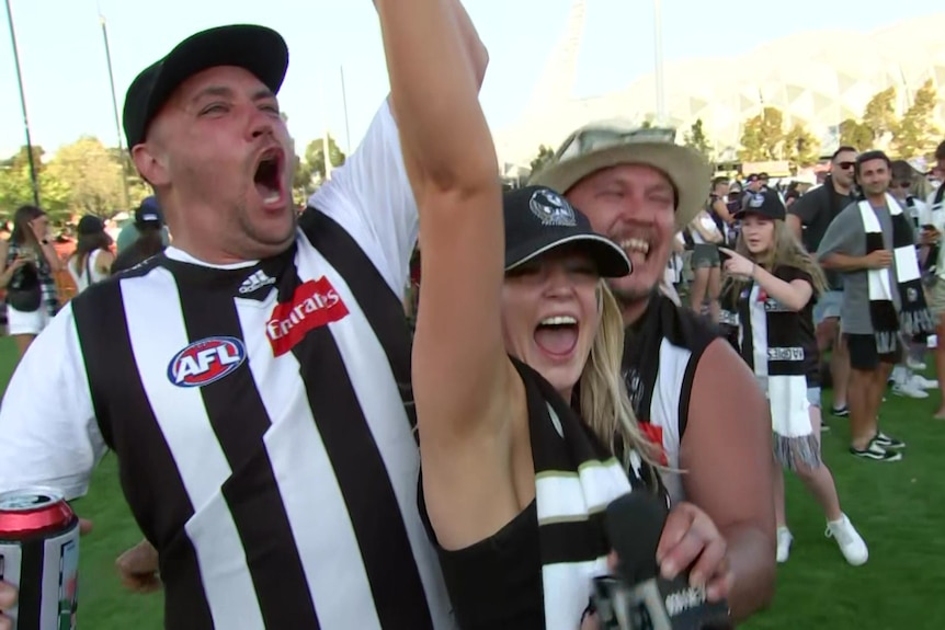 People dressed in Collingwood attire celebrate.