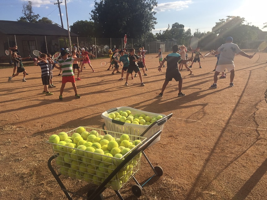 Children holding tennis rackets on a clay tennis court.