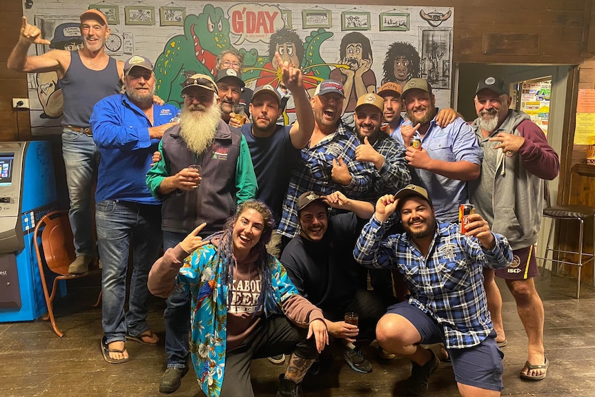 A group of happy people holding beers smile together at an outback pub.