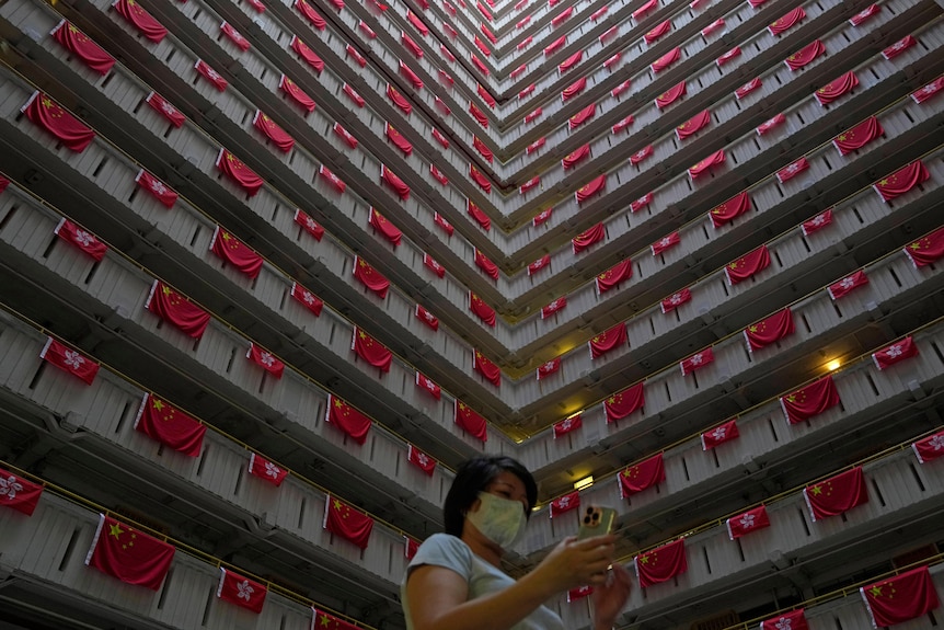 A woman walks past the Chinese and Hong Kong flags hanging from a residential building 