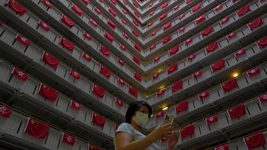 A woman walks past the Chinese and Hong Kong flags hanging from a residential building 