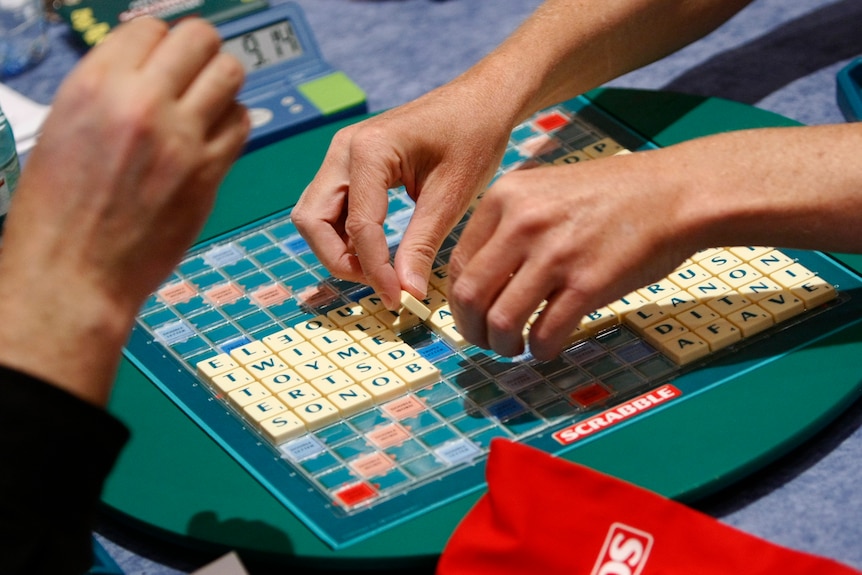 Hands move over a scrabble board covered in tiles 
