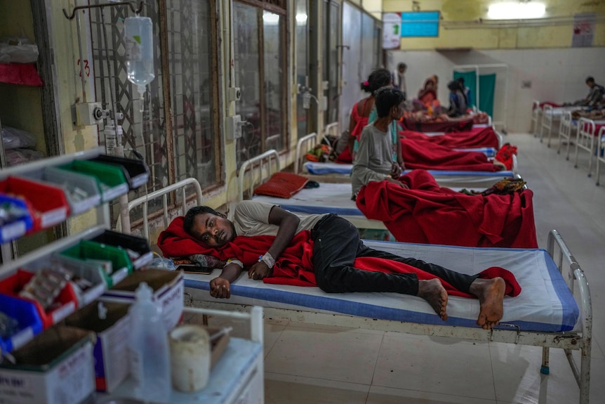 A sickle cell patient sits in a bed among a row of hospital beds and clutches a red blanket