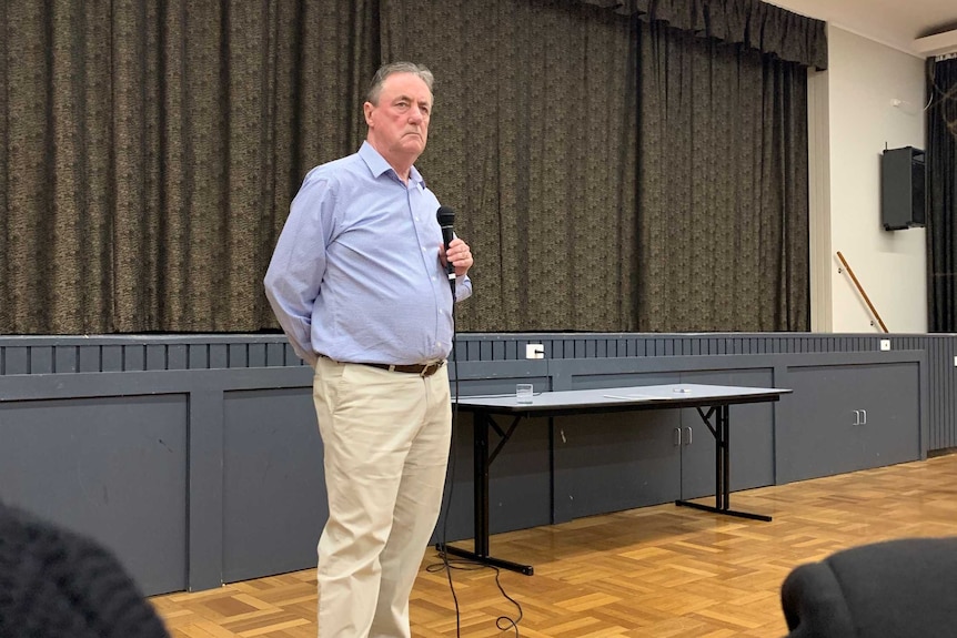 Mick Keelty holds a microphone as he looks out into a room