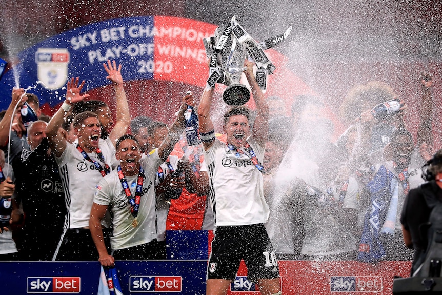 Fulham players lift a playoff trophy and spray champagne