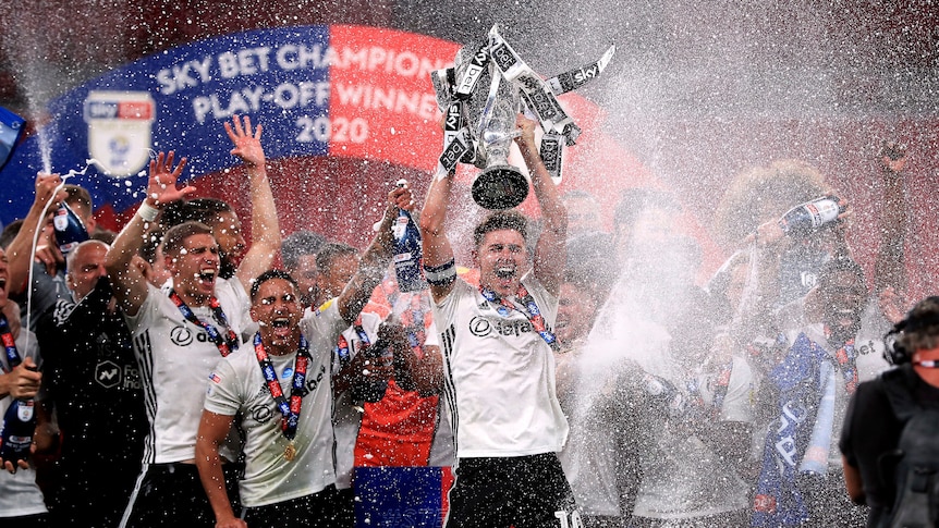 Fulham players lift a playoff trophy and spray champagne