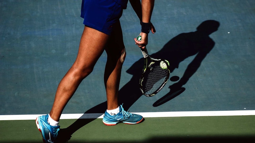 A tennis player lines up at the baseline of the court, getting ready to serve their ball.