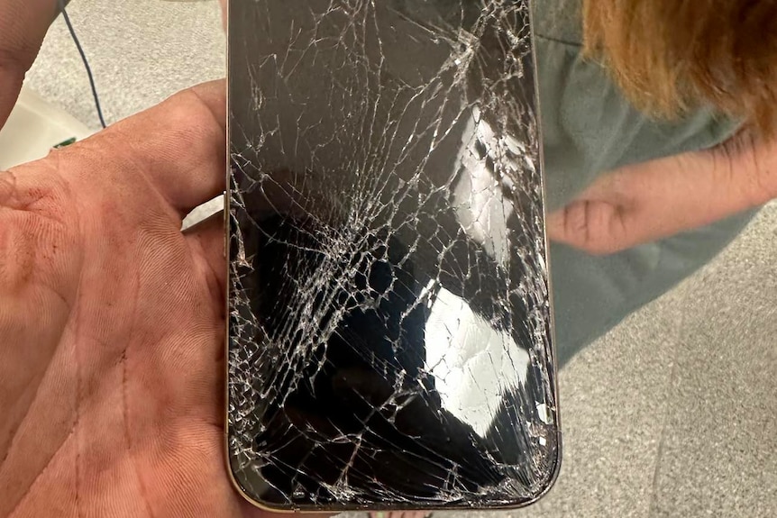 The smashed screen of a mobile phone, held in the palm of a hand.