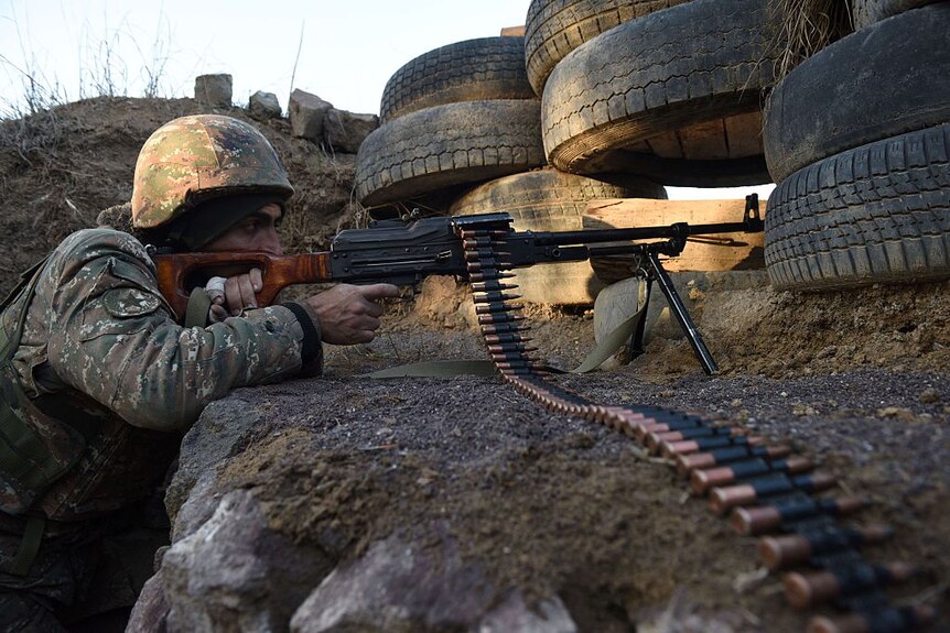 An Armenia soldier is pointing a machine gun while guarding a border post