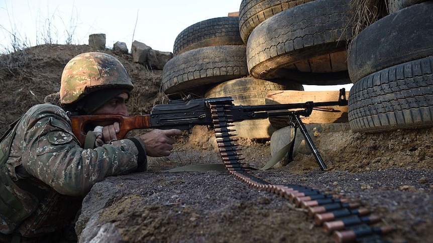 An Armenia soldier is pointing a machine gun while guarding a border post