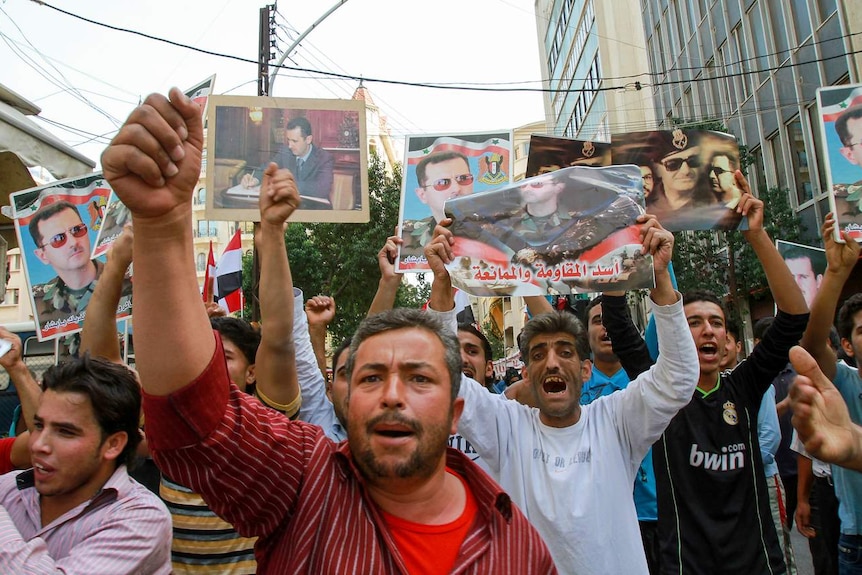 People march through the streets holding up posters of Bashar al-Assad.