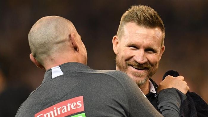 Coach Nathan Buckley smiles while receiving a hug from colleague