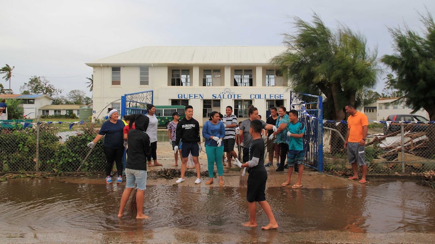 Wide shot of a group of people standing at the front of a school building.