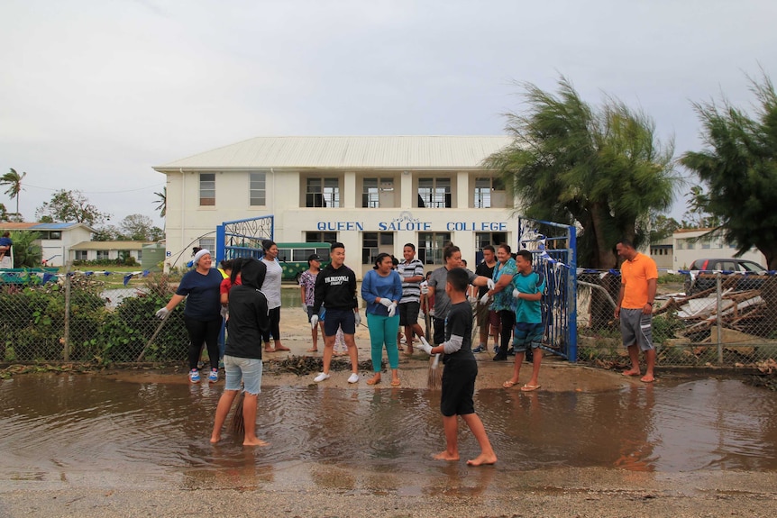 Wide shot of a group of people standing at the front of a school building.