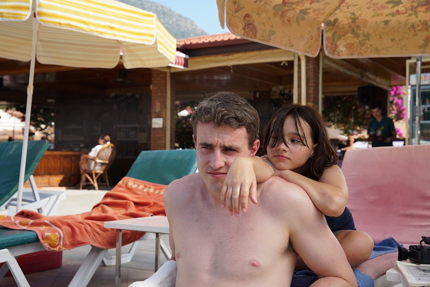 A 12 year old girl leaning on a shirtless man in his late 20s, lounging by a pool