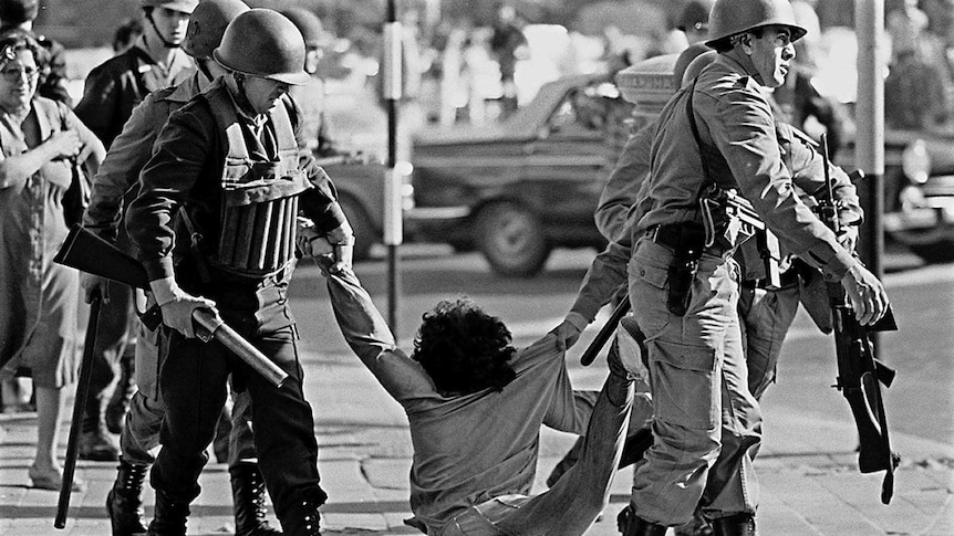 Black and white image of members of Argentina military's arresting a protester in 1982.