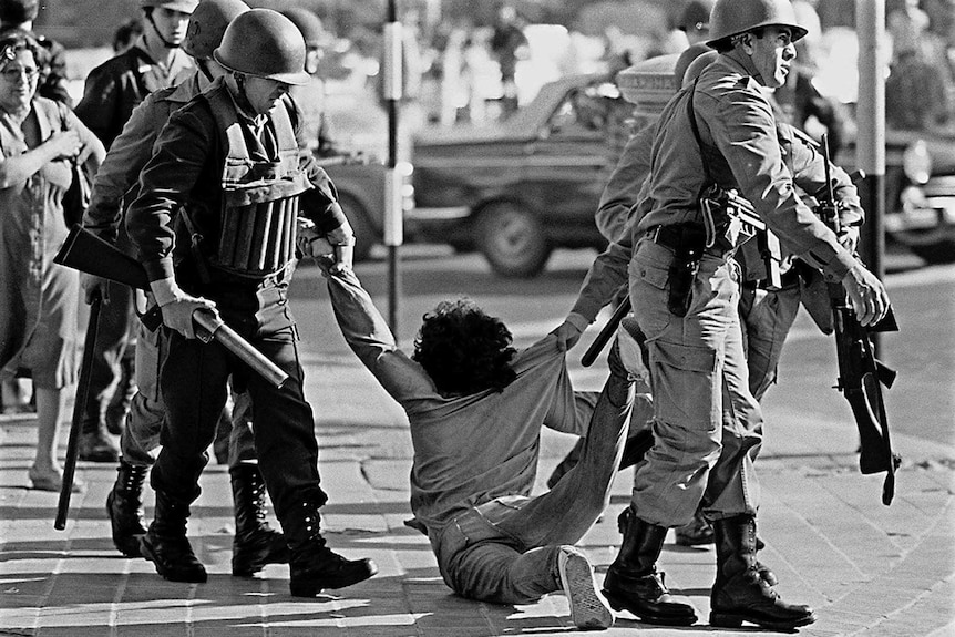 Black and white image of members of Argentina military's arresting a protester in 1982.