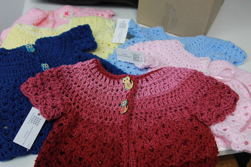 Brightly coloured knitted baby jumpers with cat and owl shaped buttons on a table.