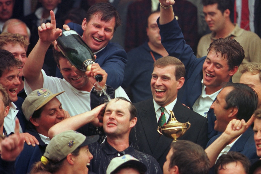 Prince Andrew laughs in a crowd as a man pours a bottle of champagne on another man's head