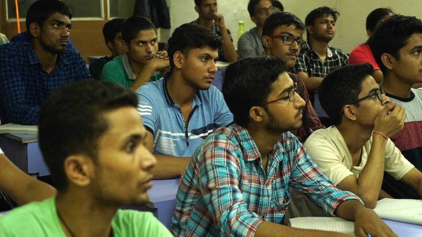 A group of Indians sit in a classroom and listen.