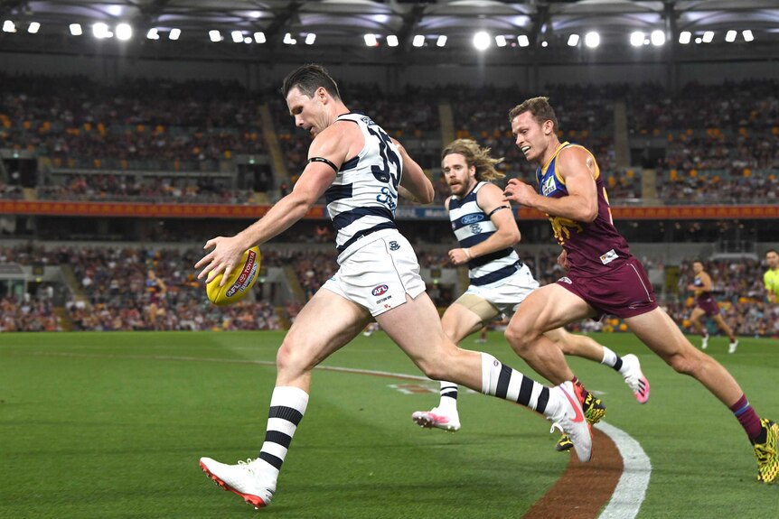 Running along the boundary line, Patrick Dangerfield drops the ball in preparation of a kick on his left foot