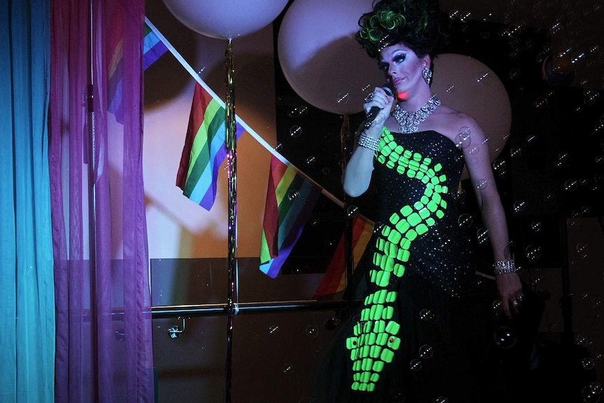 drag queen on stage with a mic and bubbles in the air