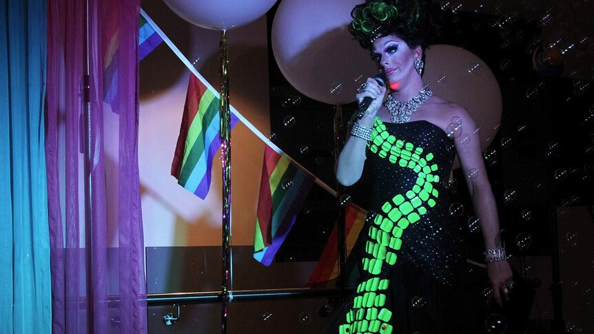 drag queen on stage with a mic and bubbles in the air