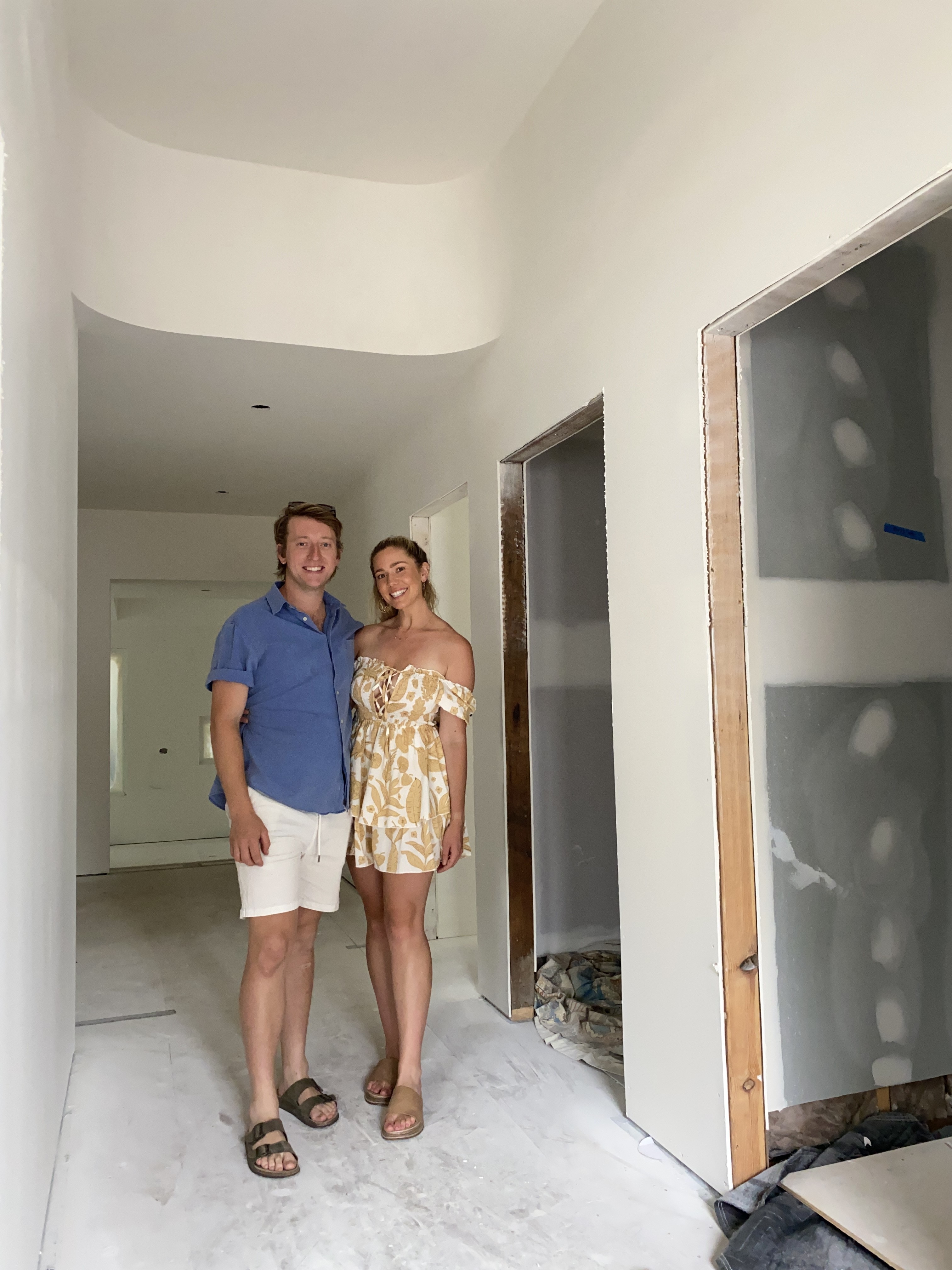 Dylan Farqhuar and Tylah Ingram standing in their house mid-renovation, there are no doors and the walls haven't been painted