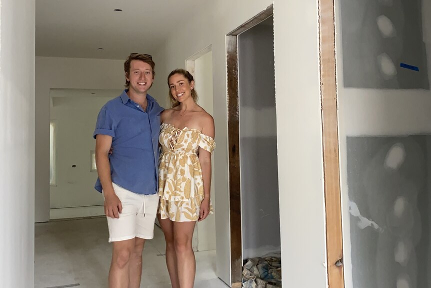 Dylan Farqhuar and Tylah Ingram standing in their house mid-renovation, there are no doors and the walls haven't been painted