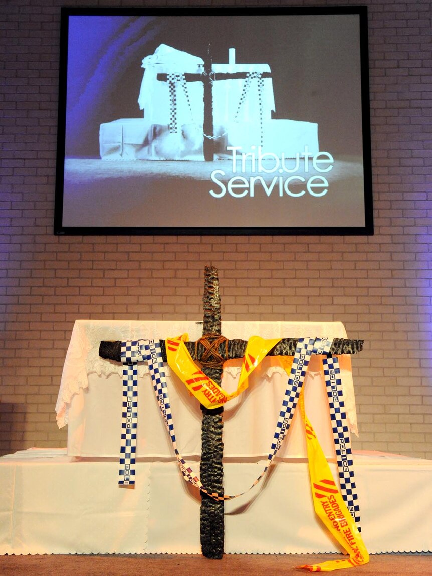 A cross, made of charred timber from the Quakers Hill nursing home fire, stands at a memorial service.