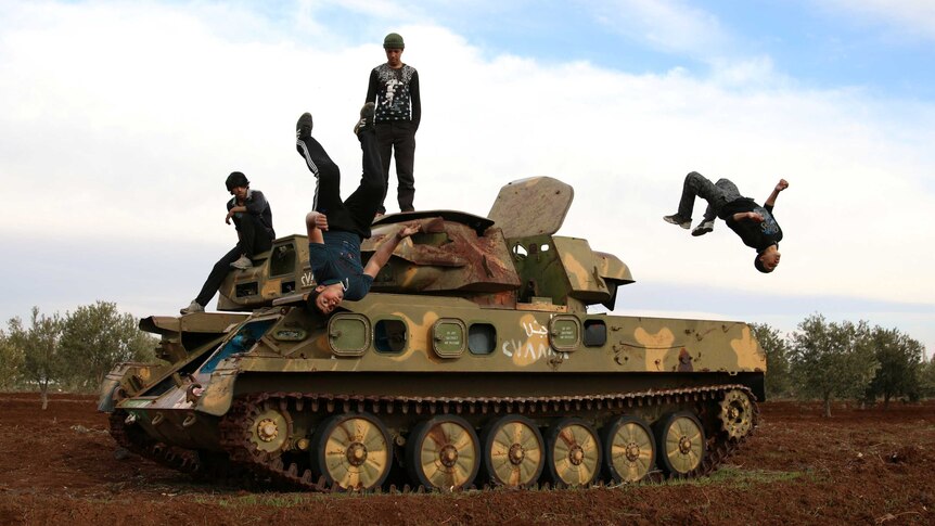 Two Syrian men flip off a military tank in the Syrian city of Inkhil.