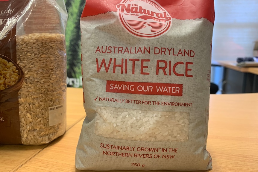 A paper pack of white rice stand on a kitchen bench. 