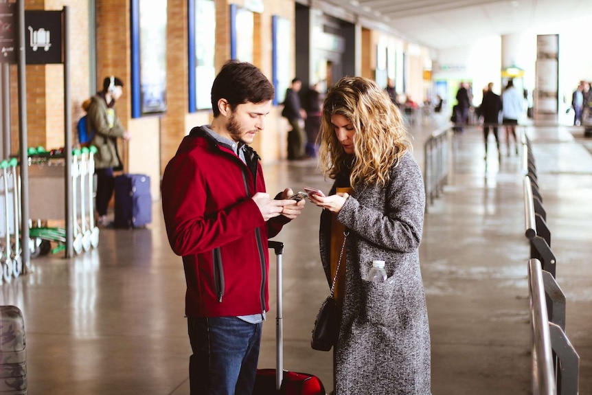 A man and woman standing in an airport looking at their phones for a story about whether rewards cards are worth it.