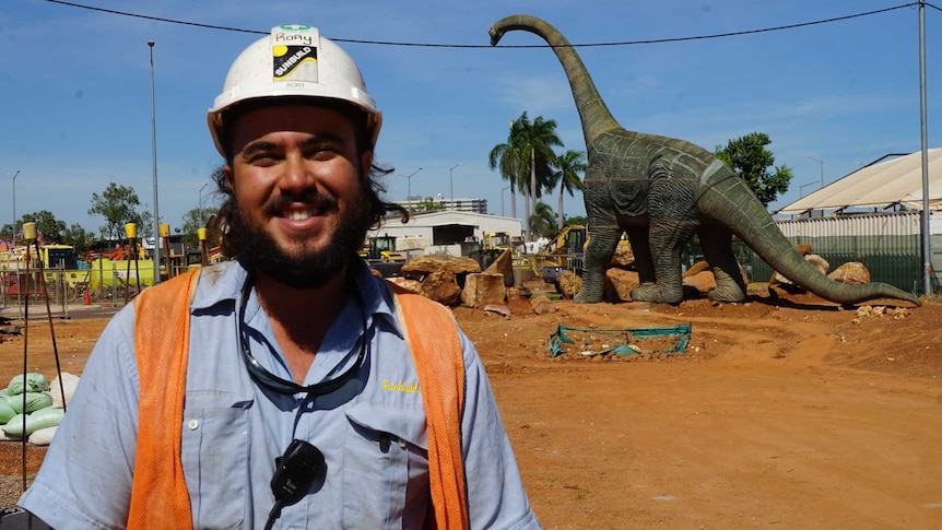 Site supervisor in hi-viz standing with fibreglass Brachiosaurus dinosaur in background on building site