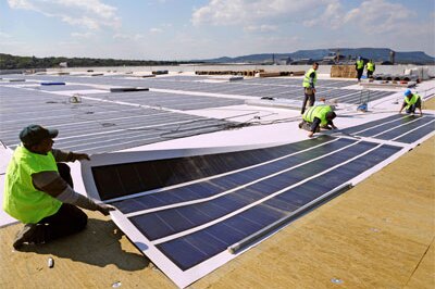 Workers in southern France unfold a roll of photovoltaic solar panels on a roof of a warehouse