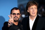 Ringo Starr (left) holds his hands in a peace sign, standing next to Paul McCartney at a movie premiere