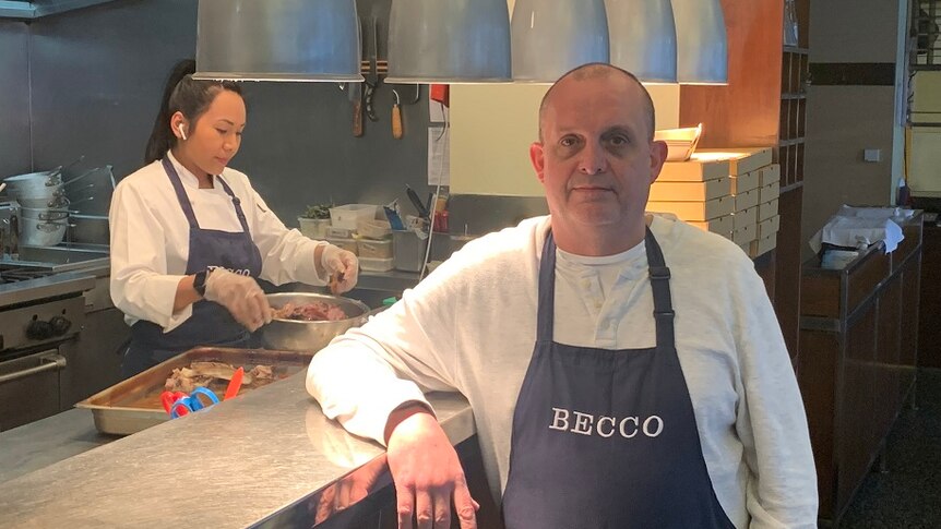 Simon Hartley stands in a 'Becco' branded apron in front of the kitchen of his restaurant.