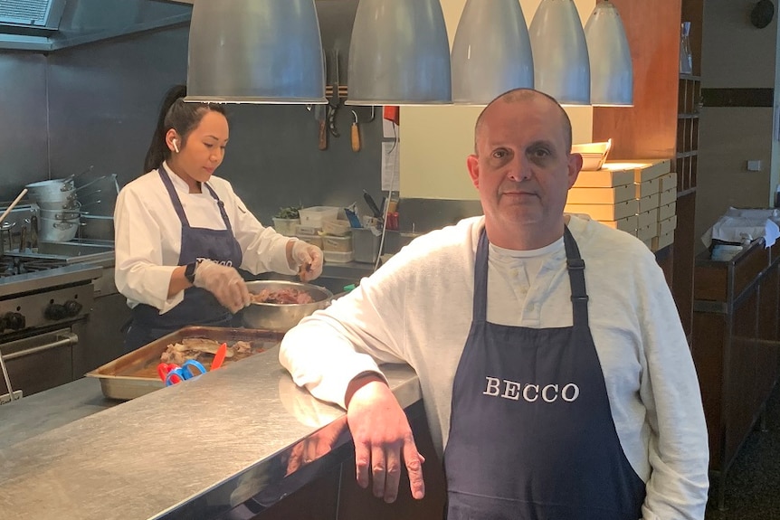 Simon Hartley stands in a 'Becco' branded apron in front of the kitchen of his restaurant.