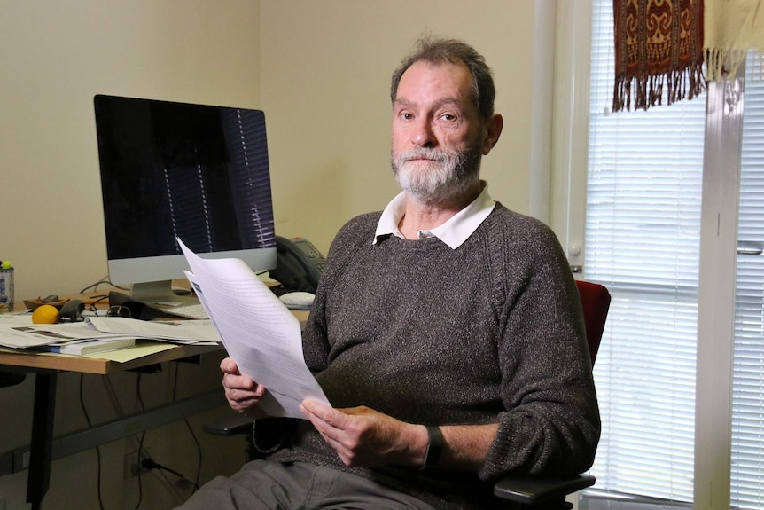 Rod Broadhurst sits at his desk holding papers.