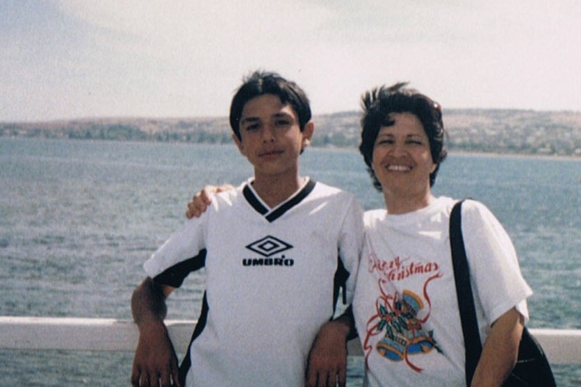 Arman Abrahimzadeh and his mother standing against a fence with the ocean behind them. 