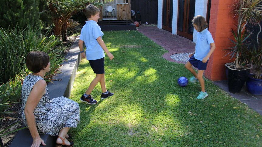 The two children kick a ball as their mother watches on.